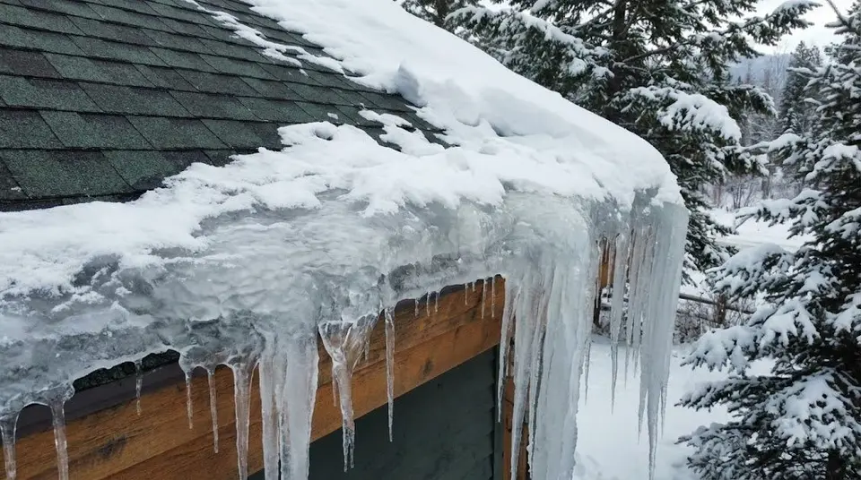 Ice dam and icicles forming along a snowy roof eave